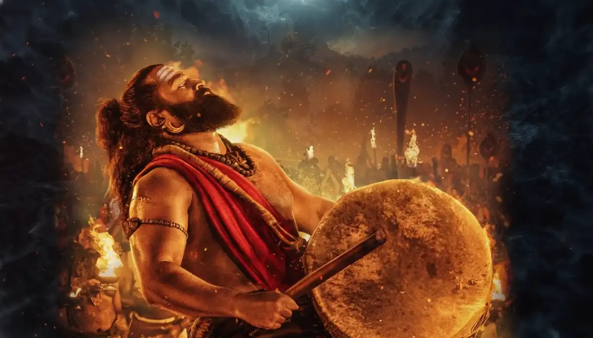 ಕಾಂತಾರ ಚಾಪ್ಟರ್ 1 - ರಿಷಬ್ ಶೆಟ್ಟಿ ಡ್ರಮ್ ಬಾರಿಸುತ್ತಿರುವ ಚಿತ್ರ, ಬೆಂಕಿ ಮತ್ತು ಹೊಗೆಯ ಹಿನ್ನೆಲೆಯಲ್ಲಿ.